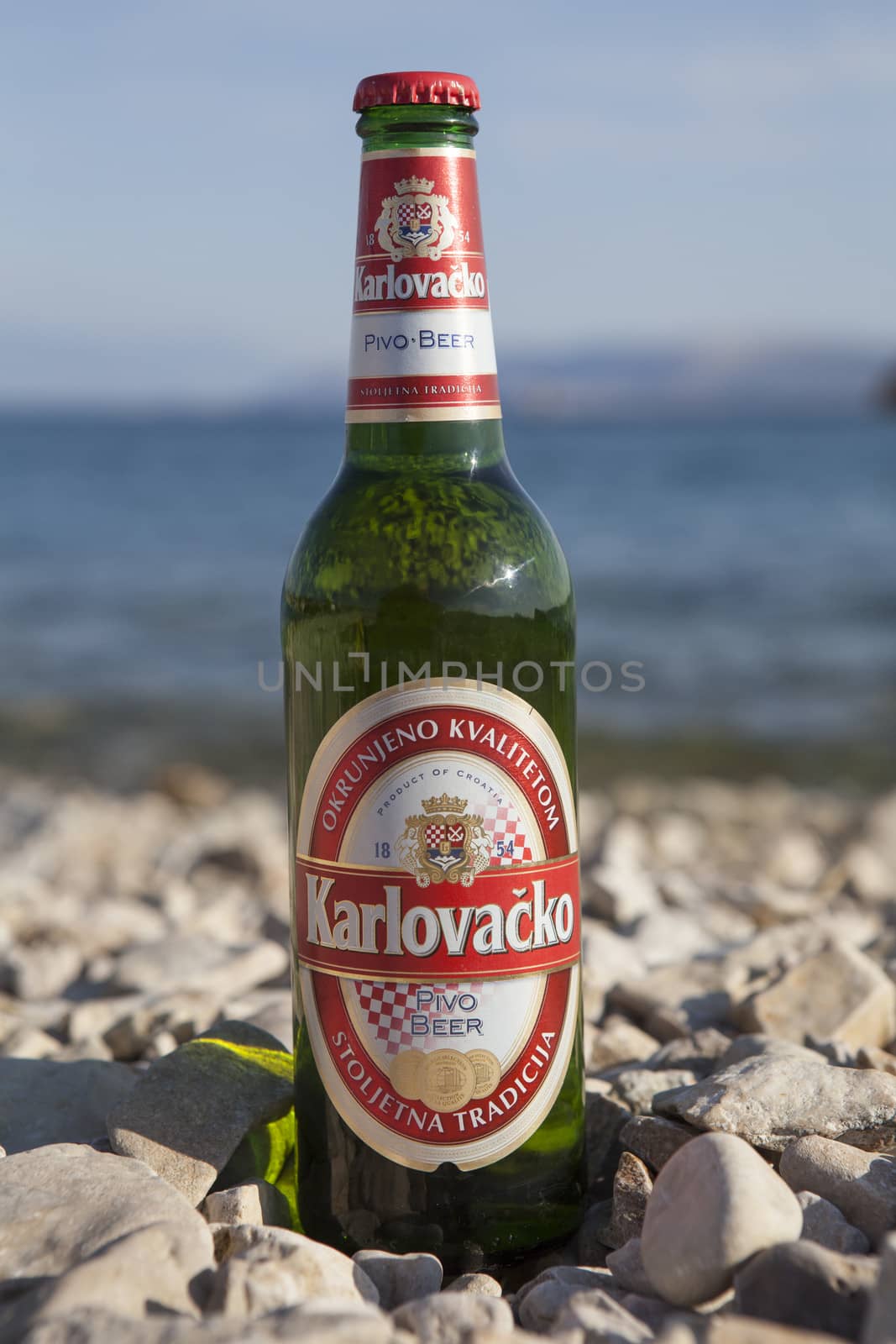 Crikvenica, Croatia – August 10, 2012: Bottle of Karlovačko, popular Croatian beer, on a pebbled beach.