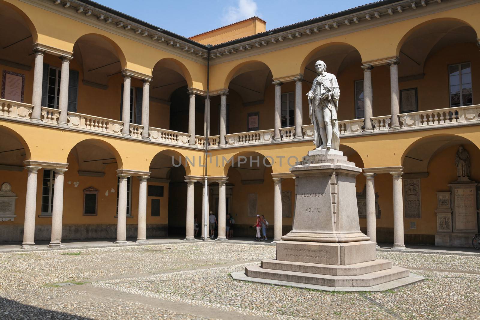 Pavia, Italy – July 9, 2013: View at the courtyard of the University of Pavia in the town of Pavia, northern Italy, with a monument of famous scientist Alessandro Volta and a group of people in the arched passageway.