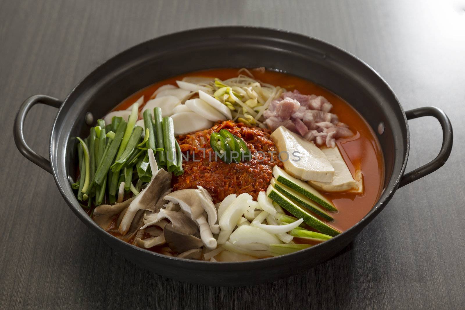 A heated stone wok of korean food with pork and mushroom