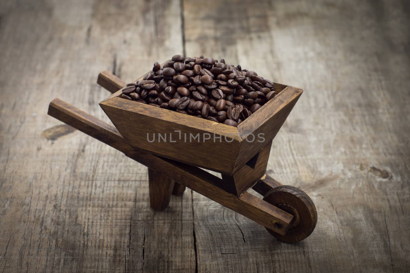 A wheelbarrow full of coffee beans on wood background