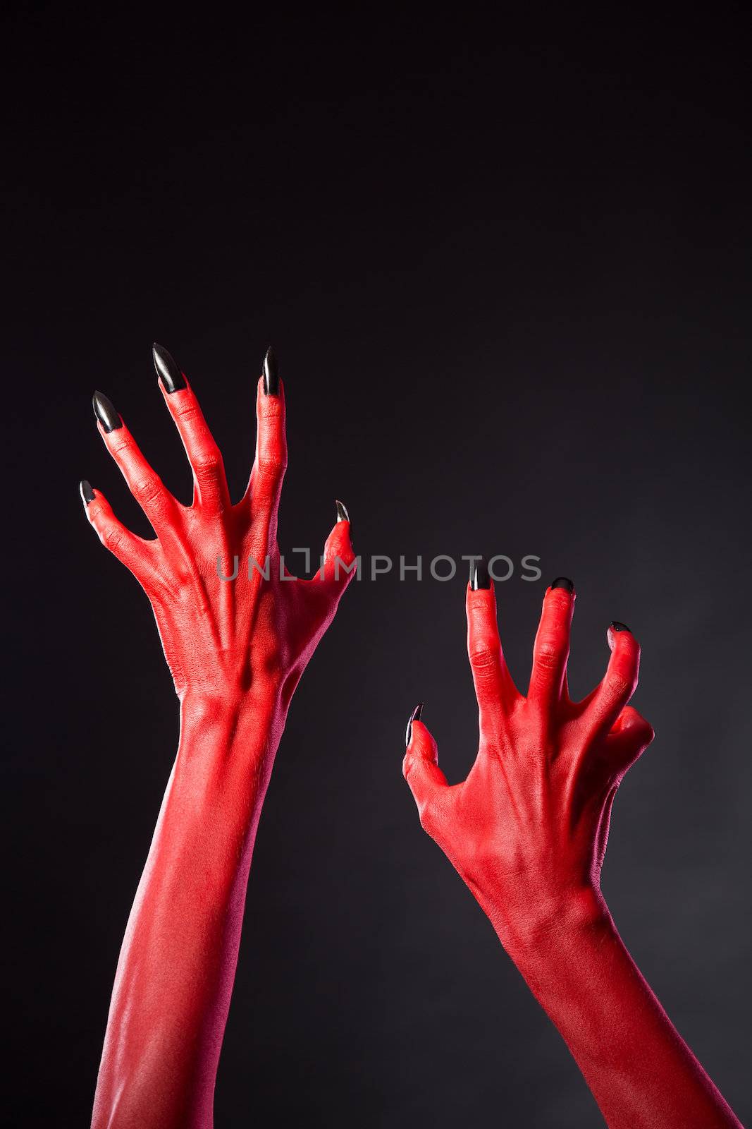 Red devil hands with black nails, Halloween theme, studio shot on black background 