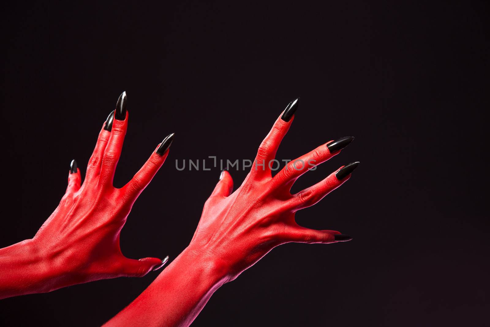 Spooky red devil hands with black nails, Halloween theme, studio shot on black background 