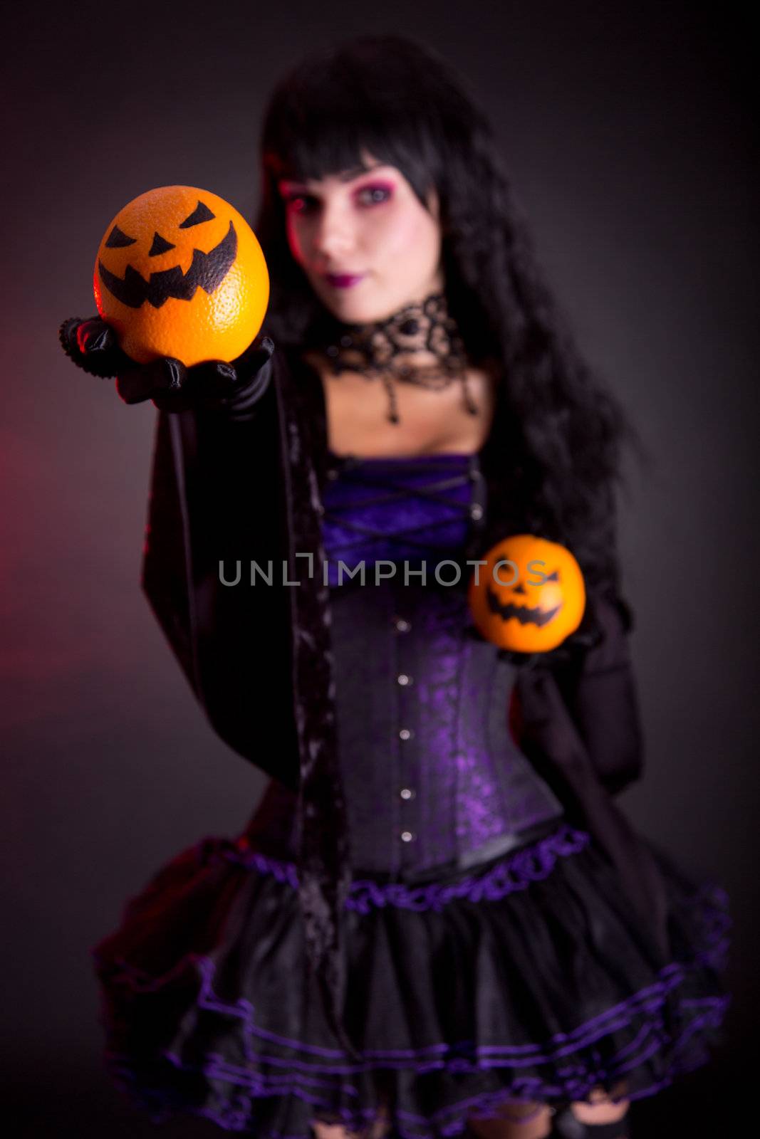 Beautiful witch in purple gothic Halloween costume with Jack lantern oranges, selective focus on fruits 