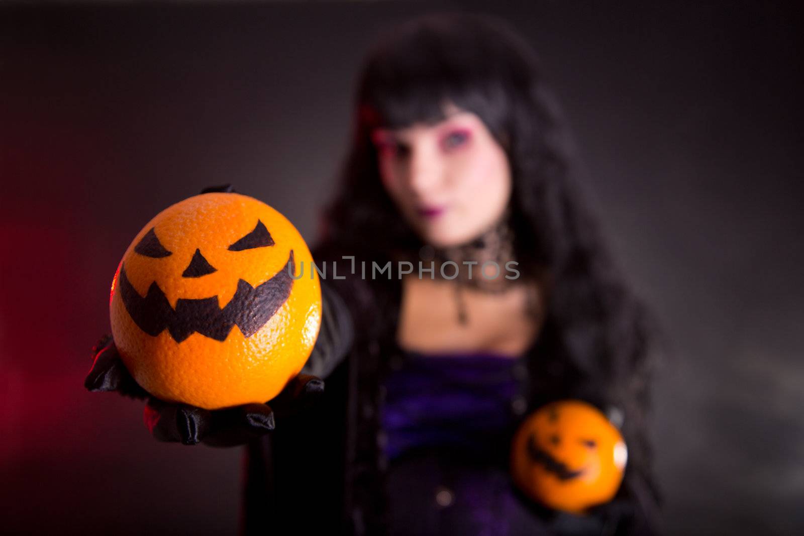 Pretty witch in purple Halloween costume with Jack lantern oranges, selective focus on fruits 