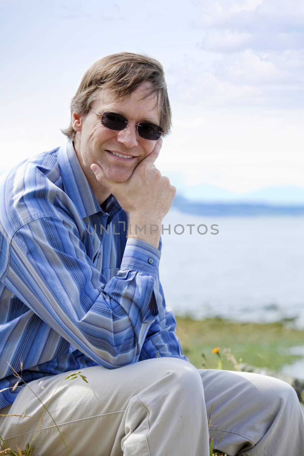 Handsome Causcasian man in forties, chin in hand,  relaxing by lake side