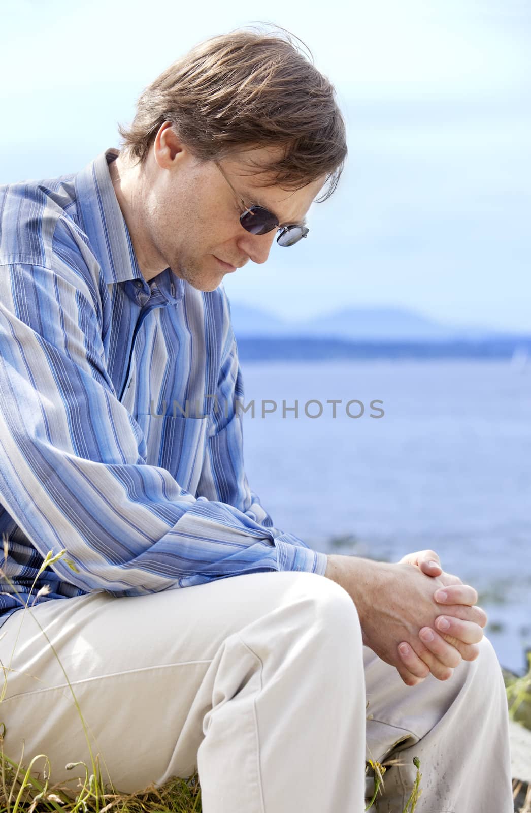Handsome Caucasian man in forties praying outdoors by side of lake