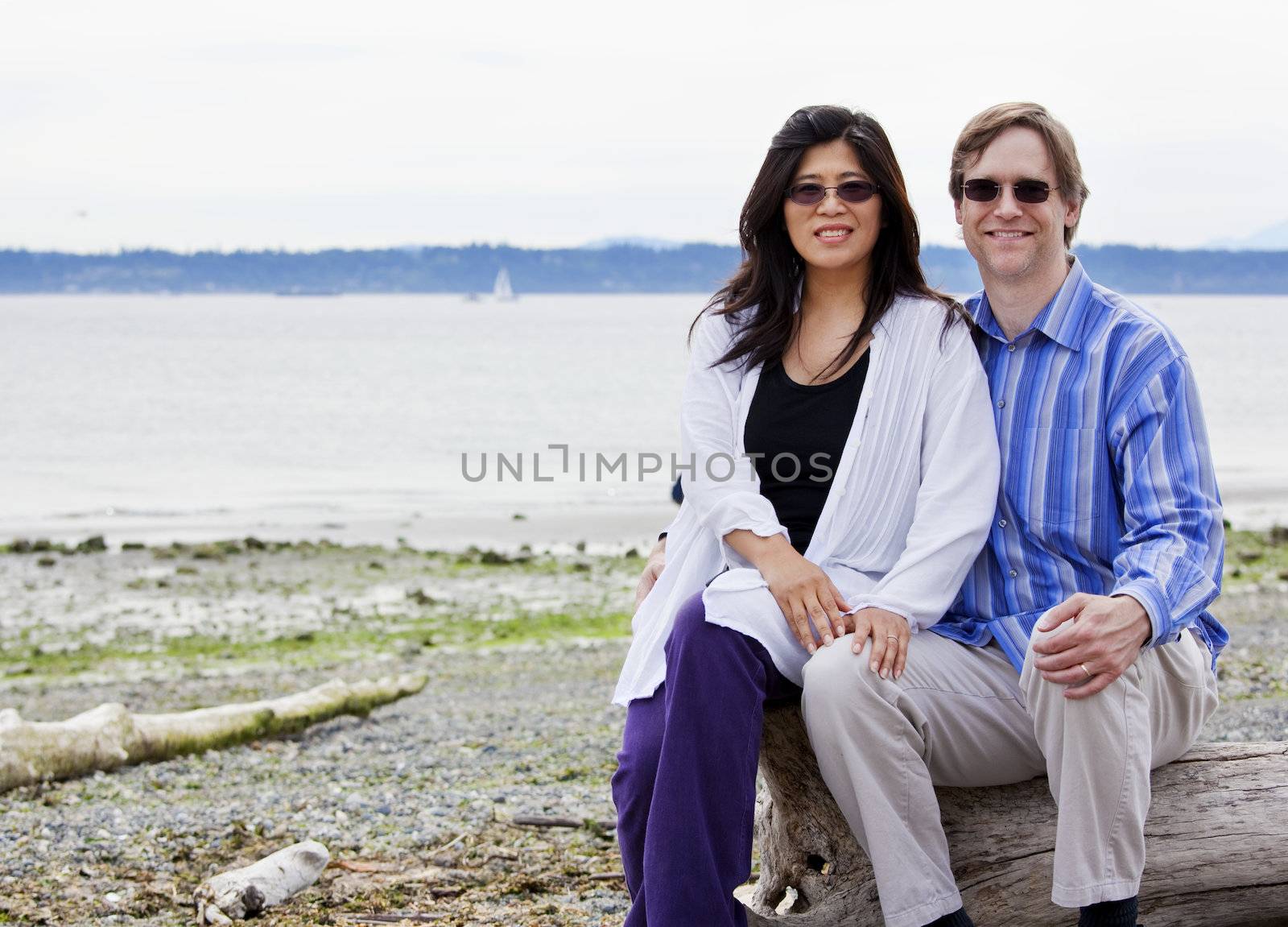 Interracial couple in forties together on beach, sitting on log by jarenwicklund