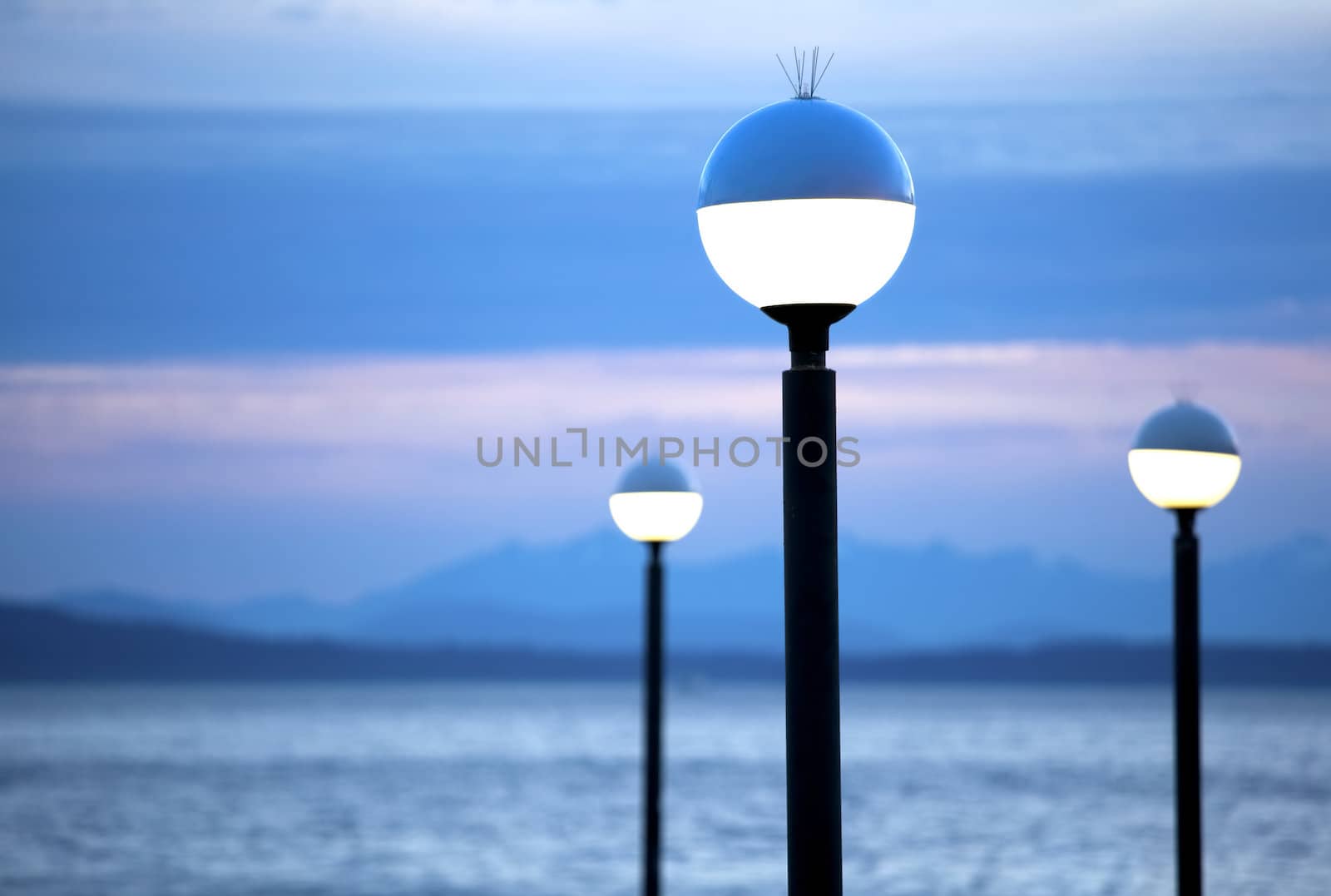 Lamp posts lit at night with blue mountain background and lake scene at dusk