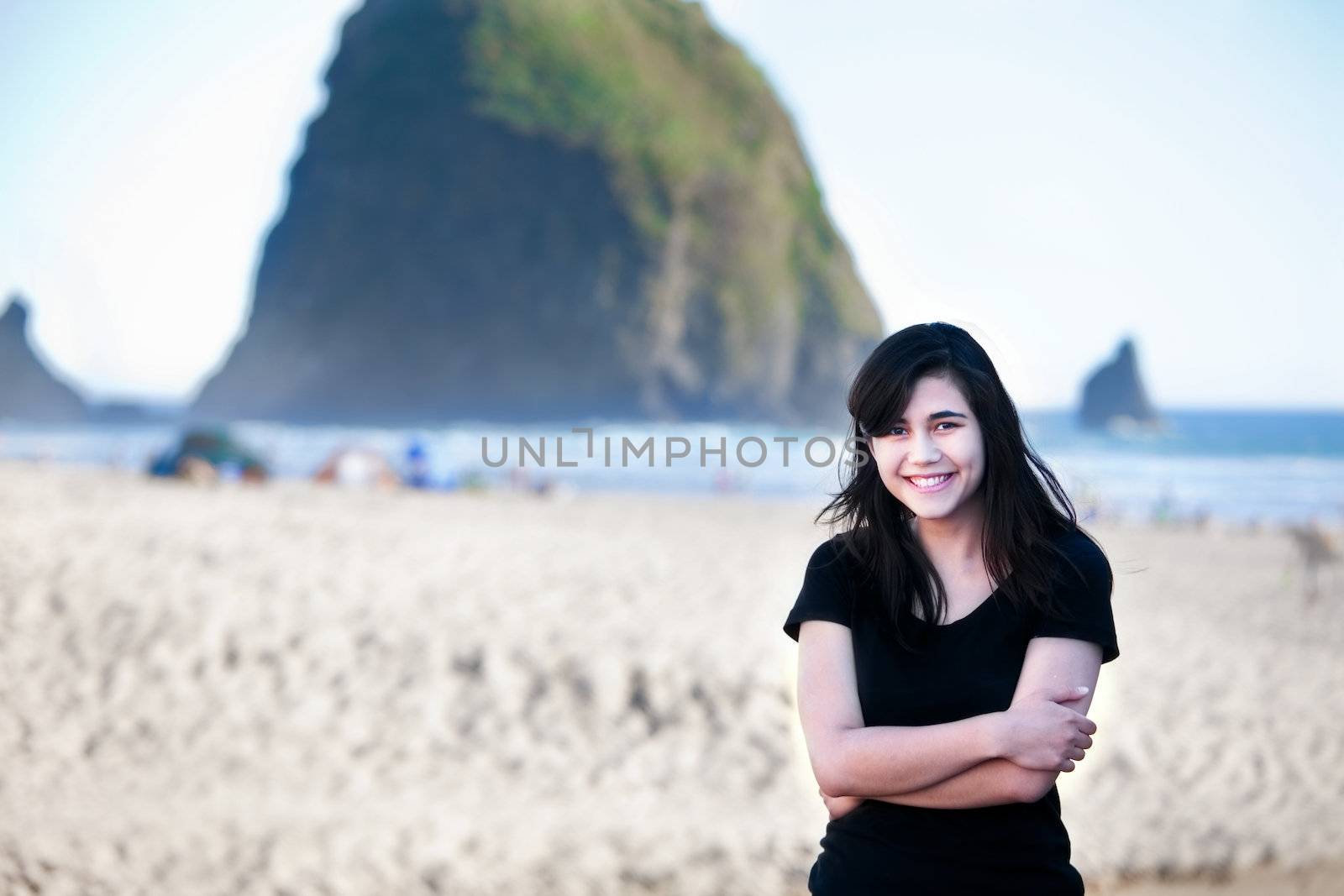 Happy biracial young woman standing on beach by Pacific Ocean with Haystack Rock in background