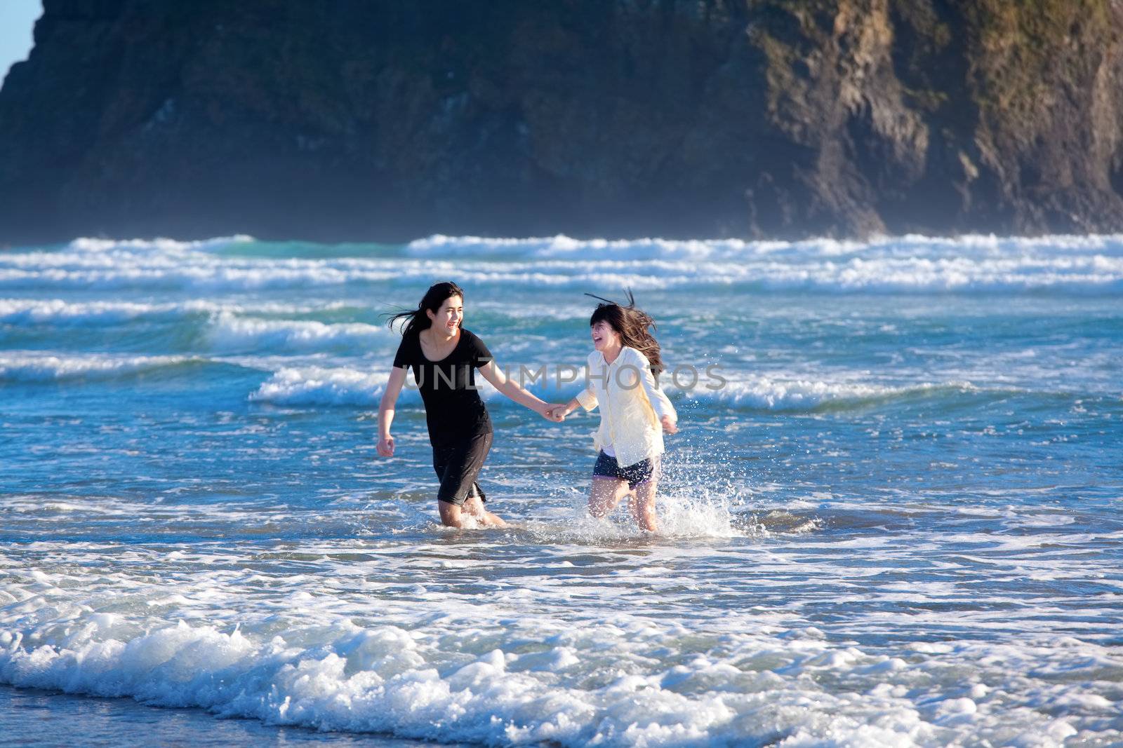 Two sisters, girls  running in the waves of the ocean together, playing