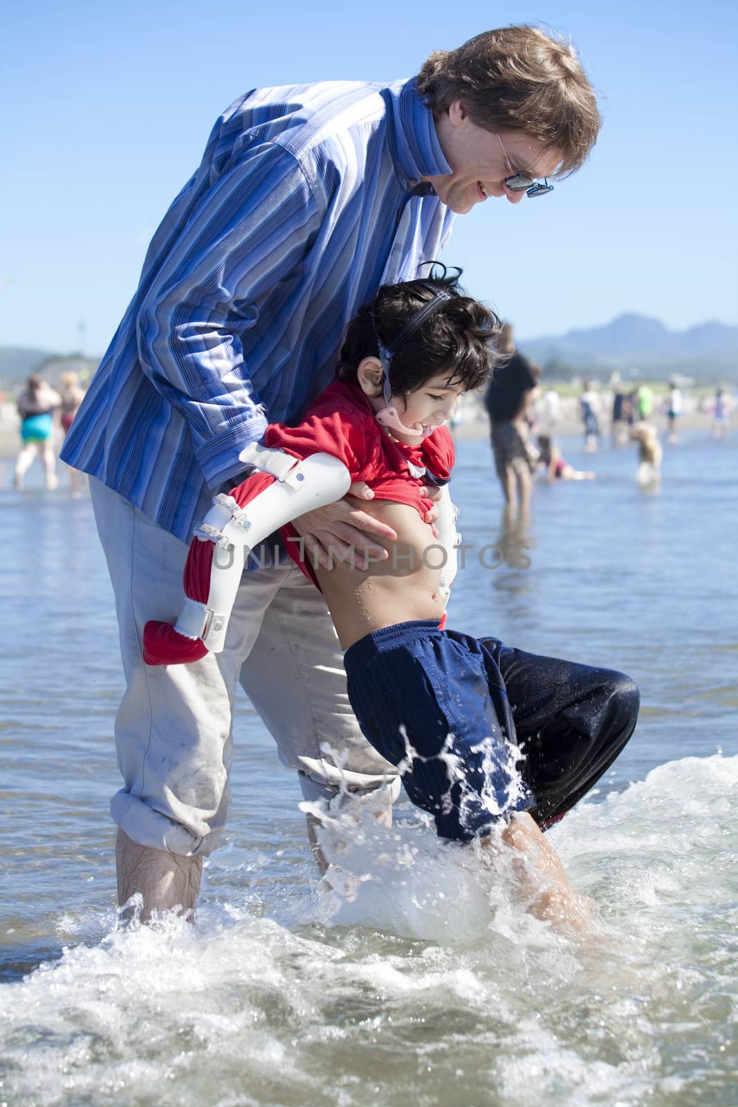 Father helping disabled son walk in the ocean waves on beach by jarenwicklund