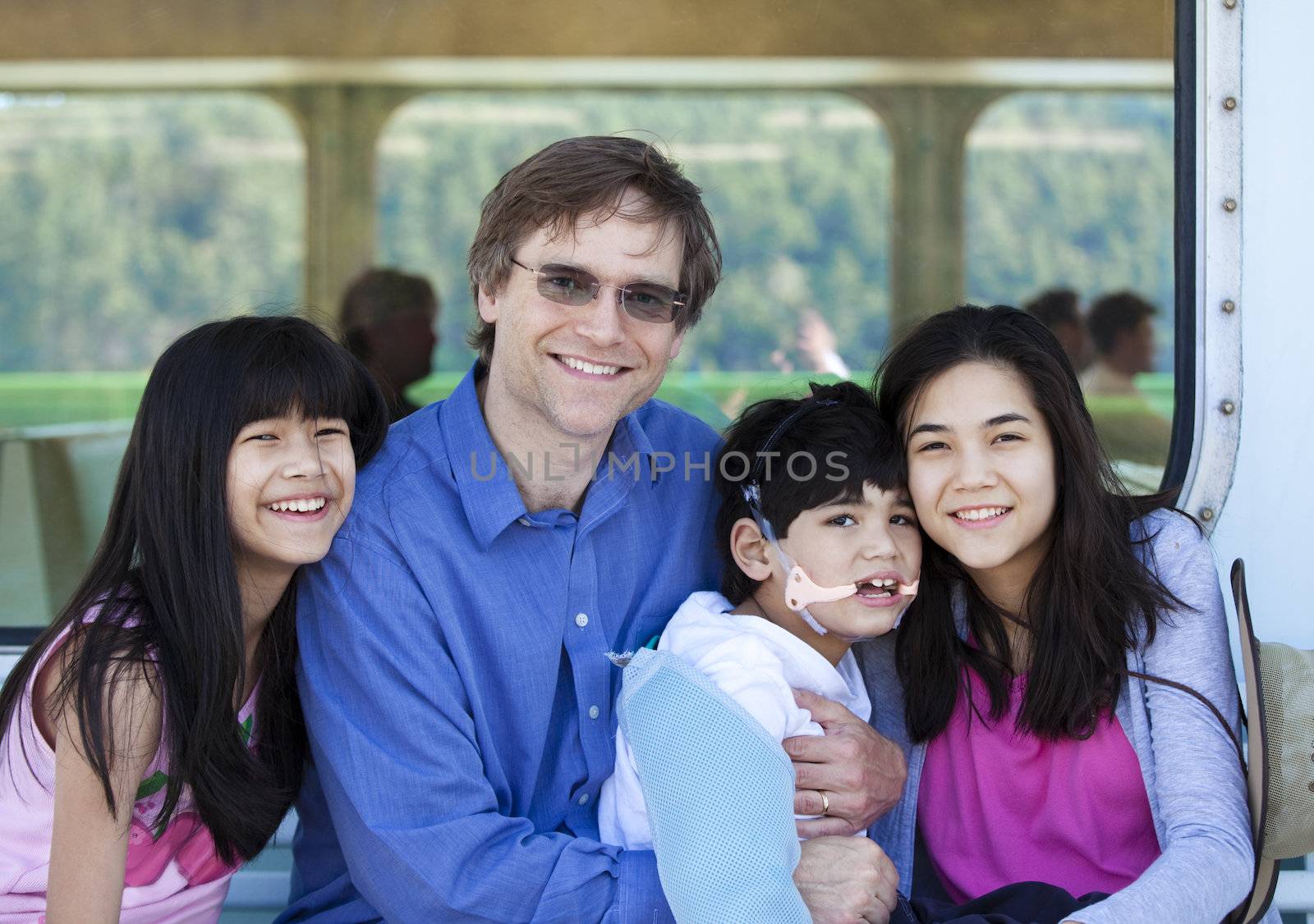 Father with his biracial children, holding disabled son on ferry boat deck. Boy has cerebral palsy