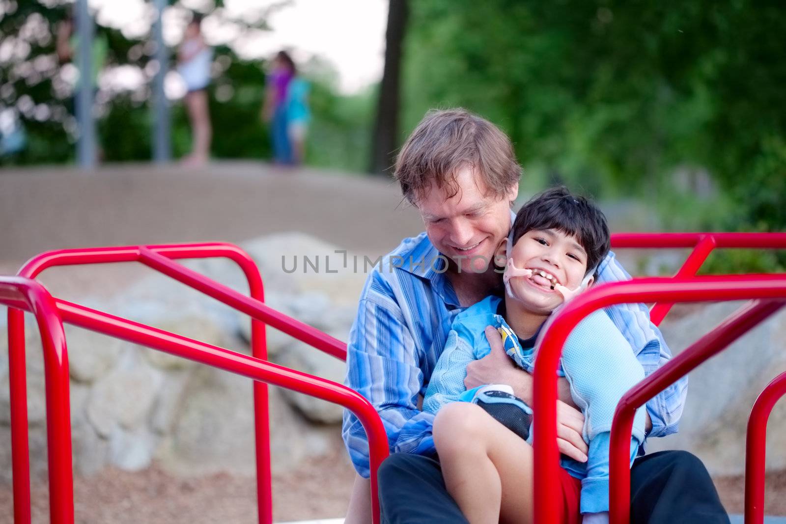 Father holding disabled son on merry go round at playground by jarenwicklund