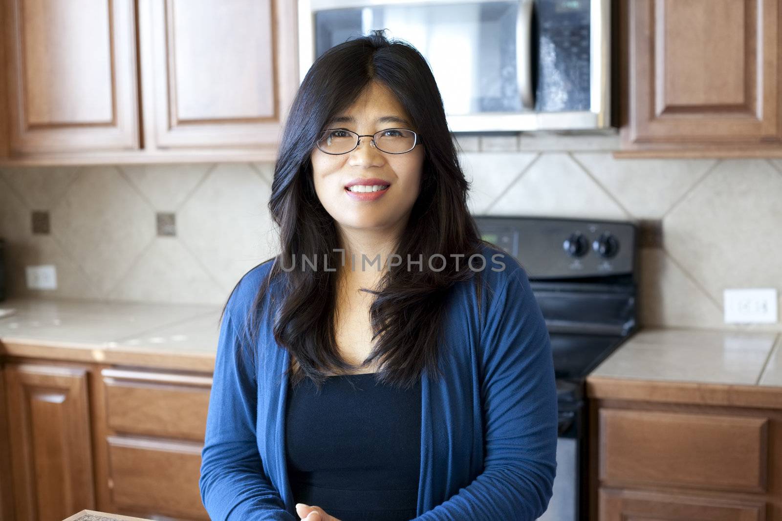 Beautiful Asian woman in early forties standing in kitchen, stove and cabinets in background