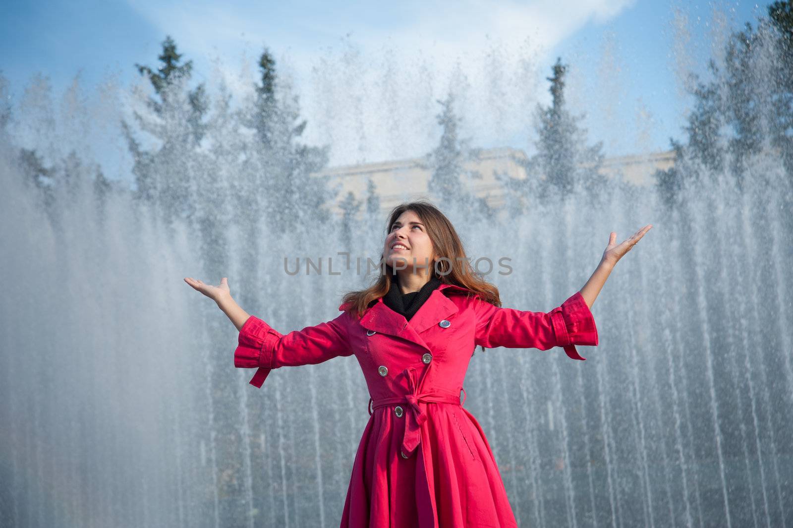 happy woman in a red cloak with his hands up at the fountain