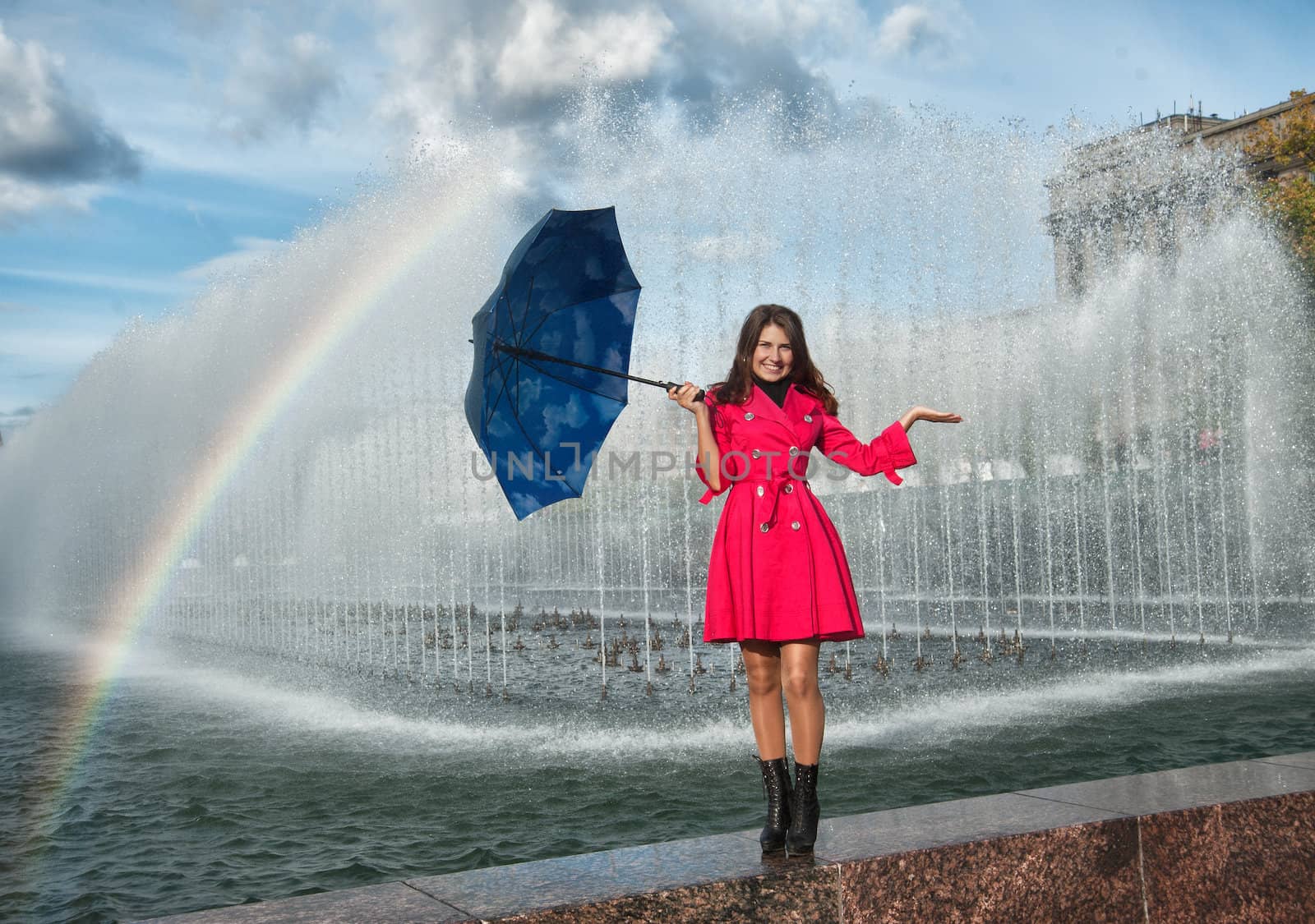 happy woman in red raincoat under the spray and rainbow