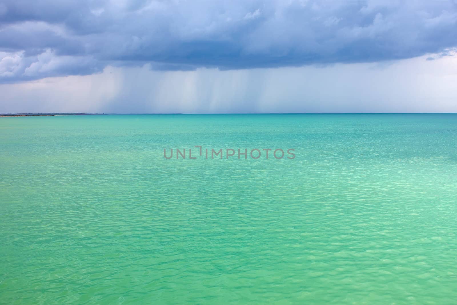 Storm clouds with rain over the sea with a turquoise surface illuminated by the sun