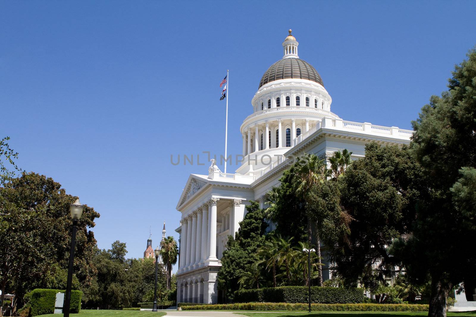 California state capitol and grounds with flags against a blue sky.