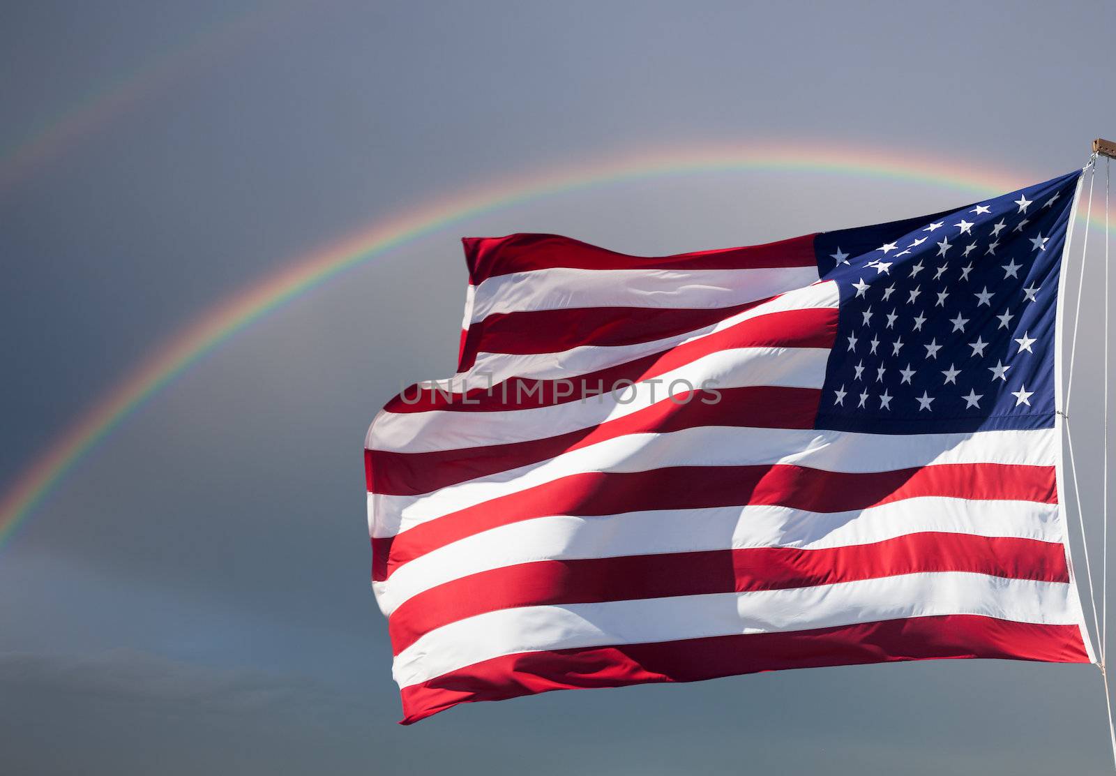 American flag waving against a cloudy sky with a rainbow