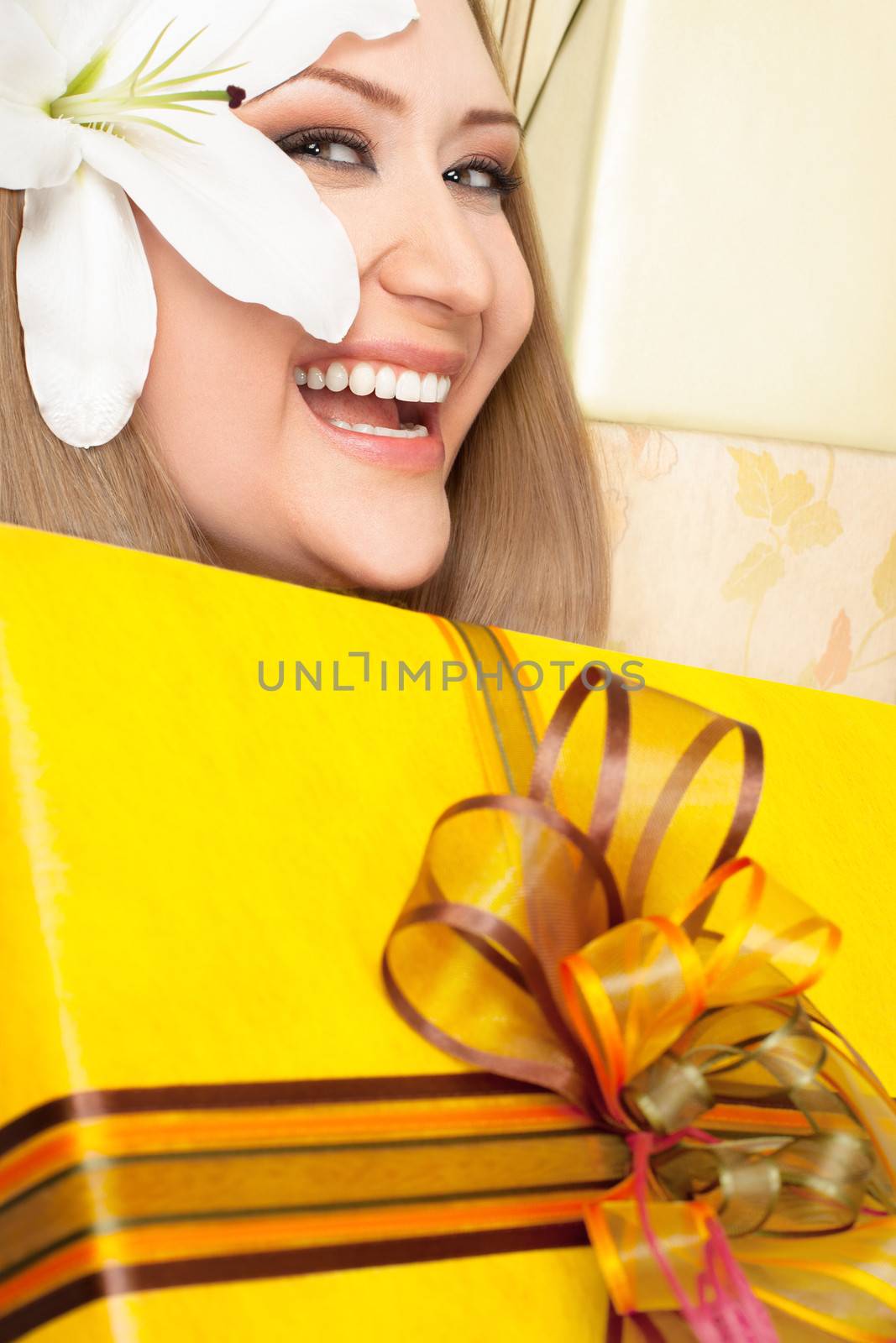 Happy puffy female with white lily in hair holding big yellow gift box