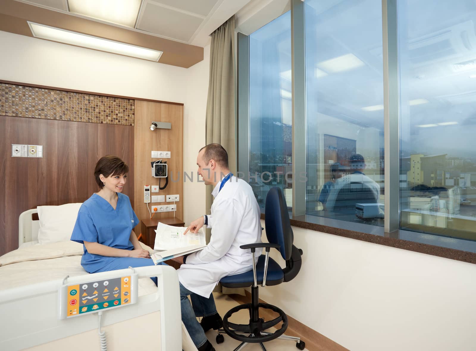 Doctor and happy healed female patient talking in hospital room