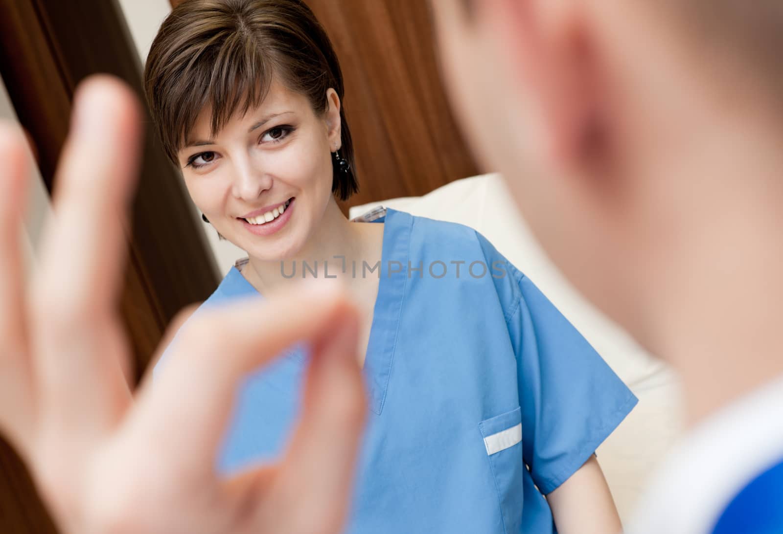 Doctor's hand showing okay gesture to healed female patient, focus on woman