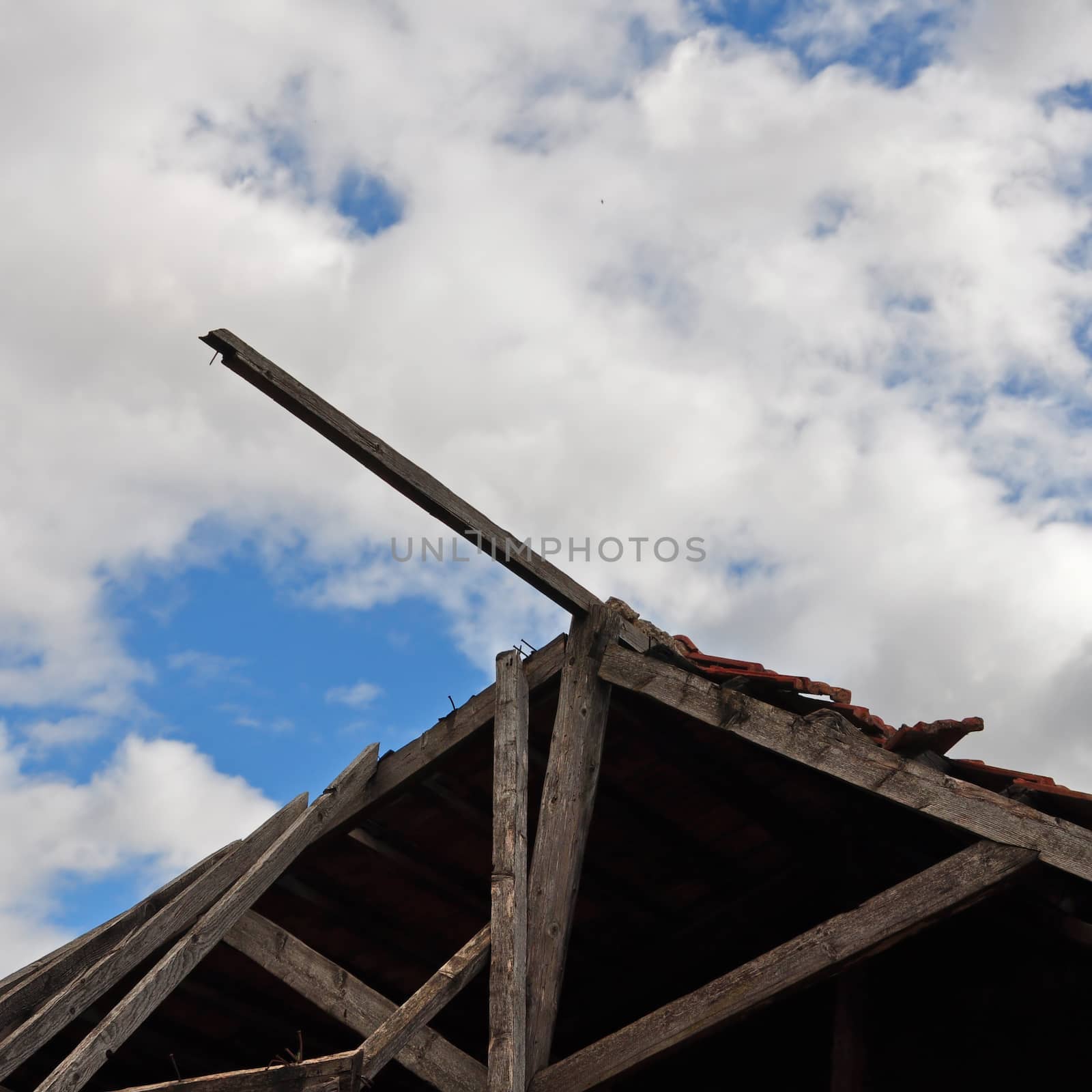 Collapsed wooden roof of an abandoned house and cloudy sky.