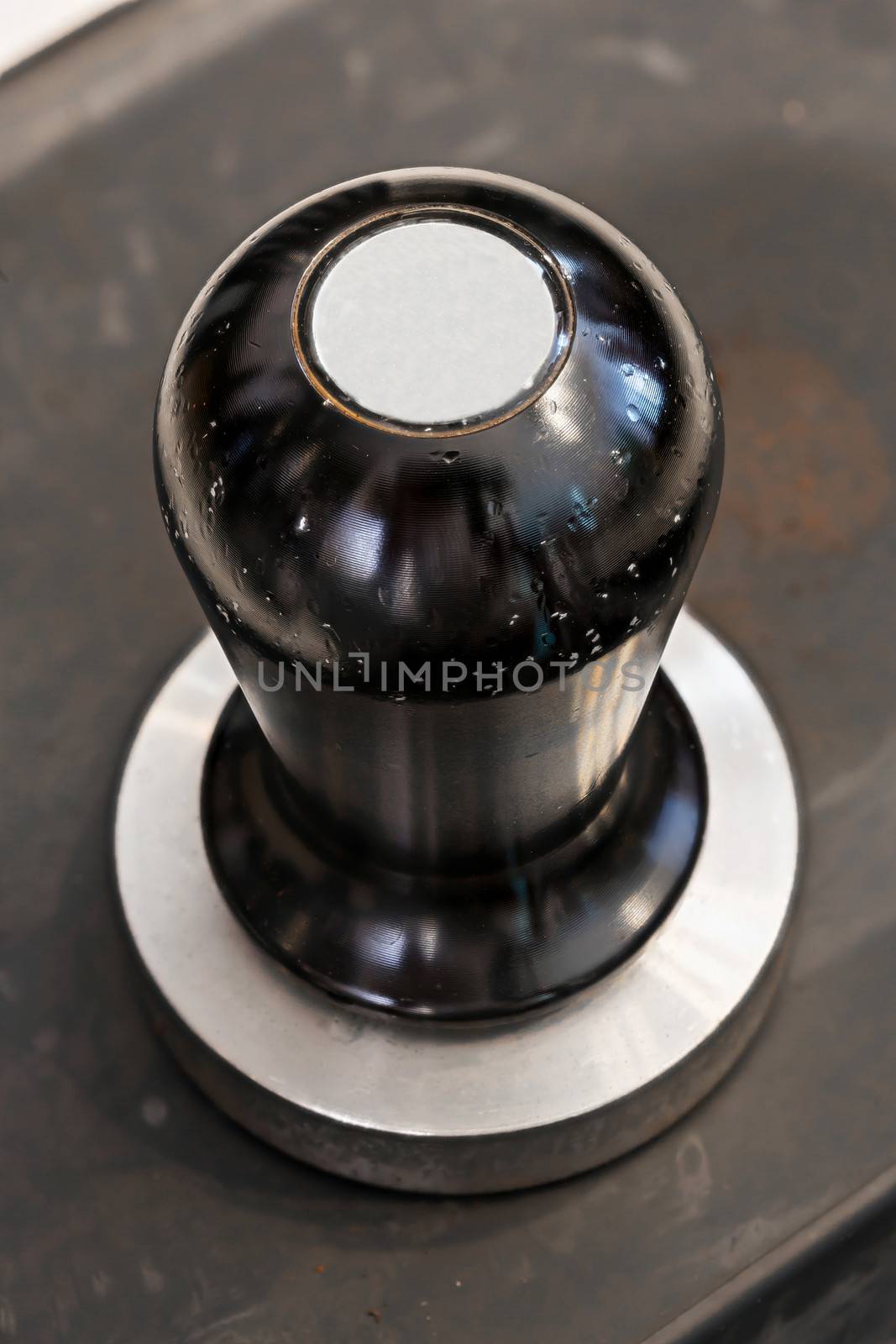 Old and stained stainless steel coffee tamper on rubber sheet