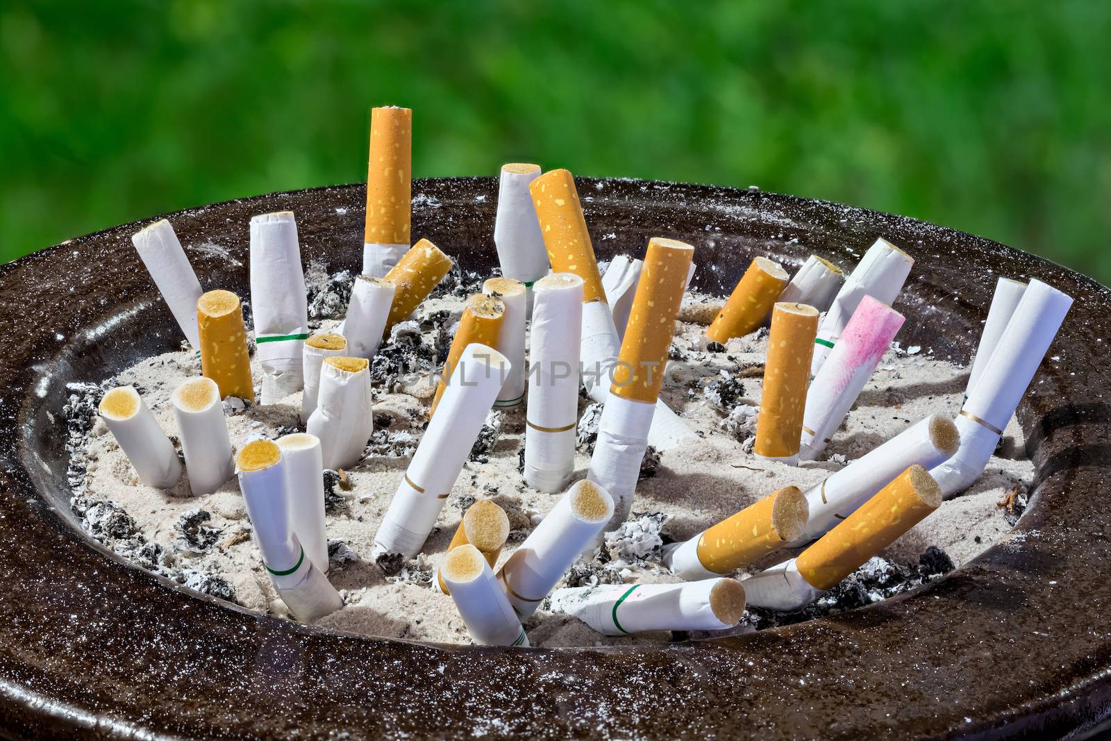 Cigarettes butt in ashtray isolated on green background