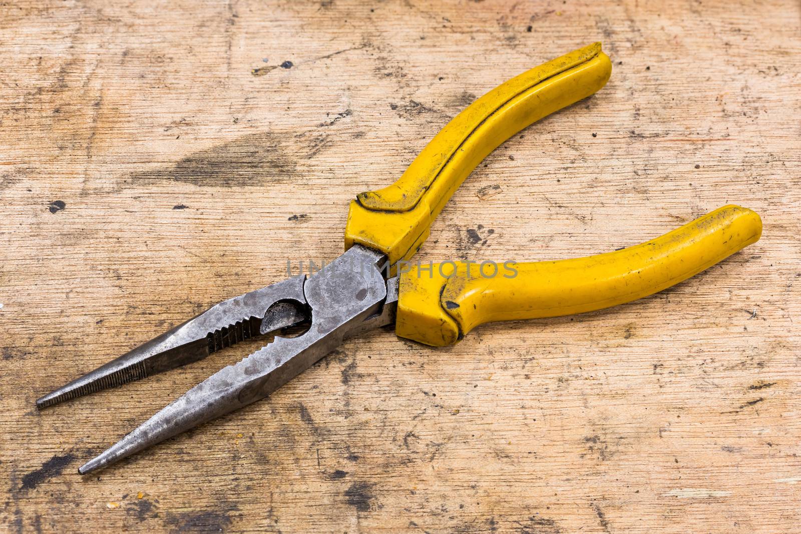 Old and dirty Needle Nose Pliers on grunge wood table