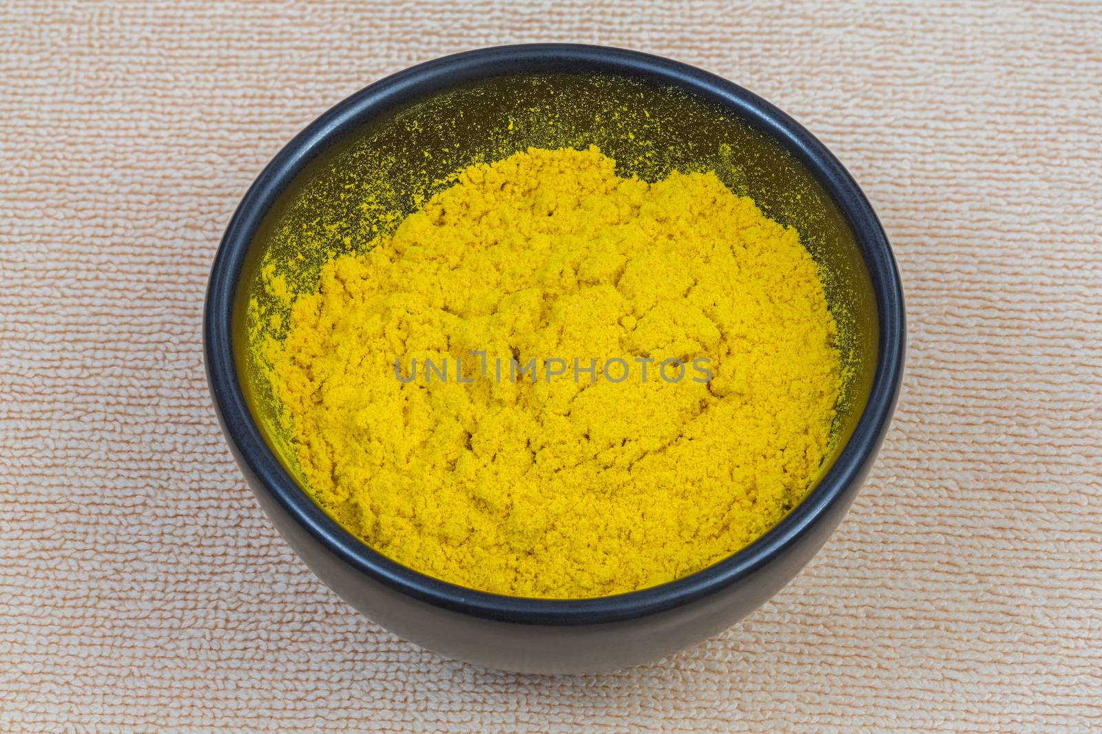 Turmeric powder in black bowl isolated on towel