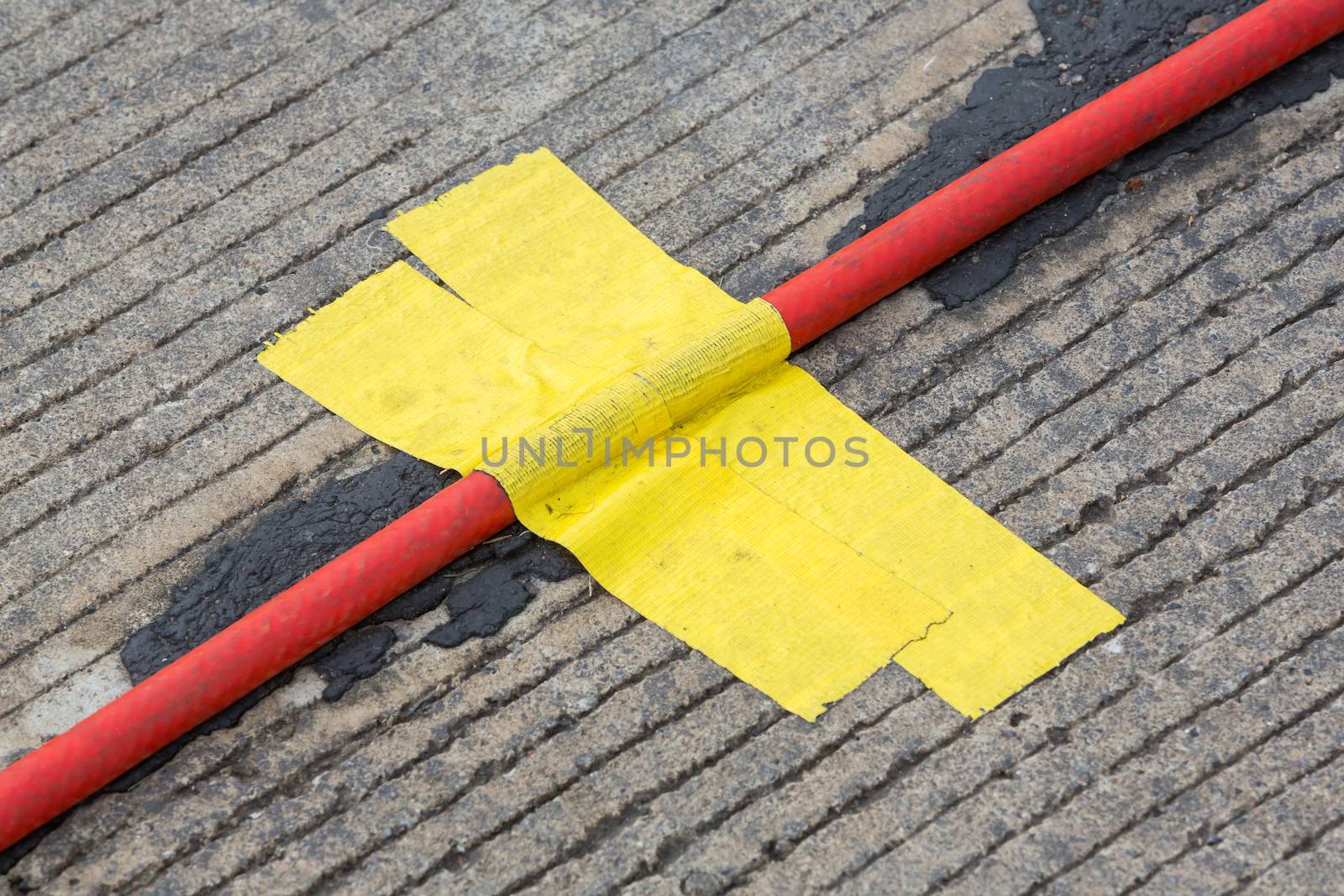Yellow cloth adhesive tape or duct tape use to stick red cable on floor