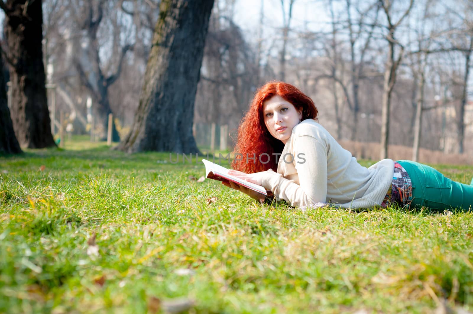beautiful red head young woman reading book in the park