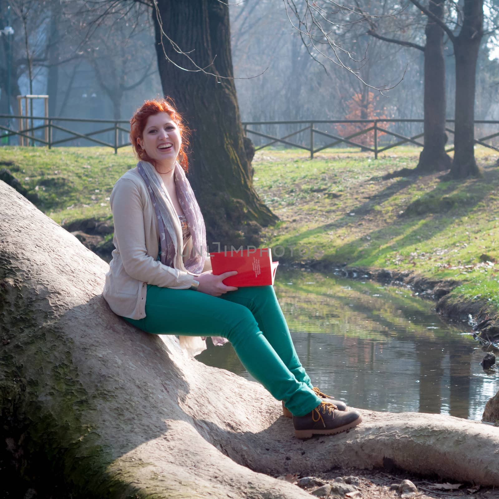 beautiful red head young woman reading book in the park