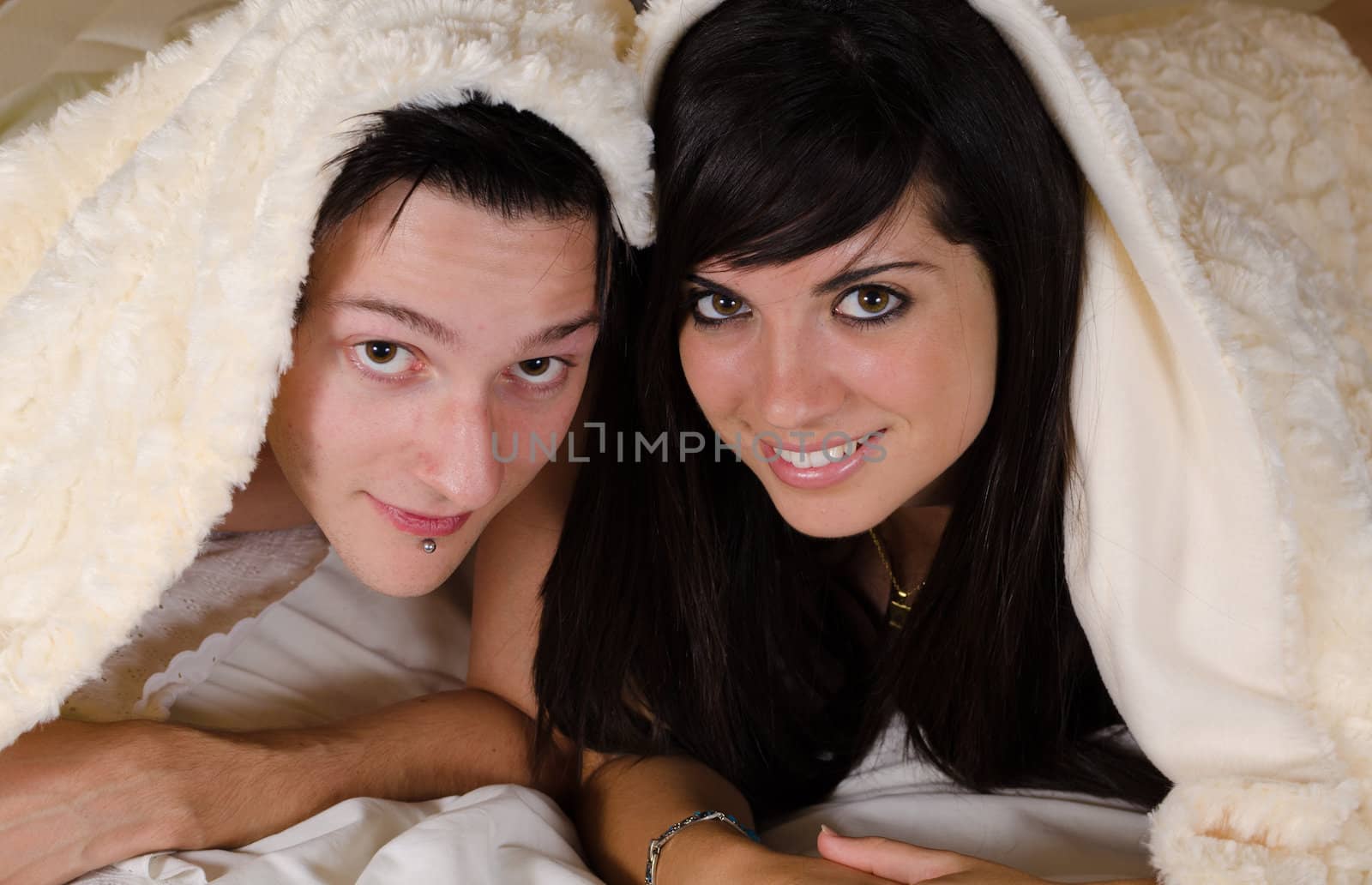 Happy couple  under a cozy blanket looking at camera