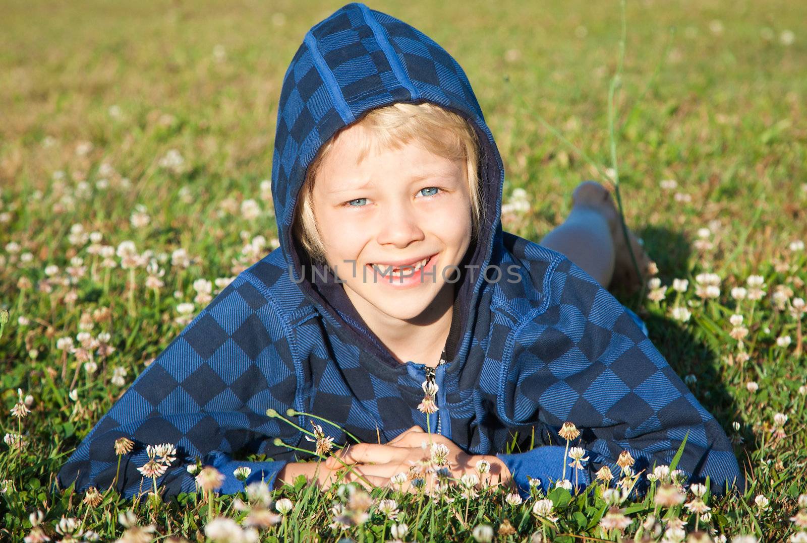 A cute happy smiling young boy with missing front teeth lying in grass with clover.