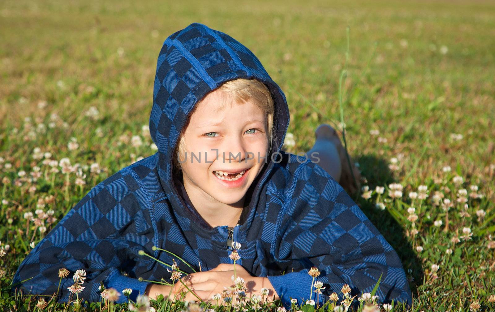 A cute happy smiling boy lying in grass with clover with missing front teeth.