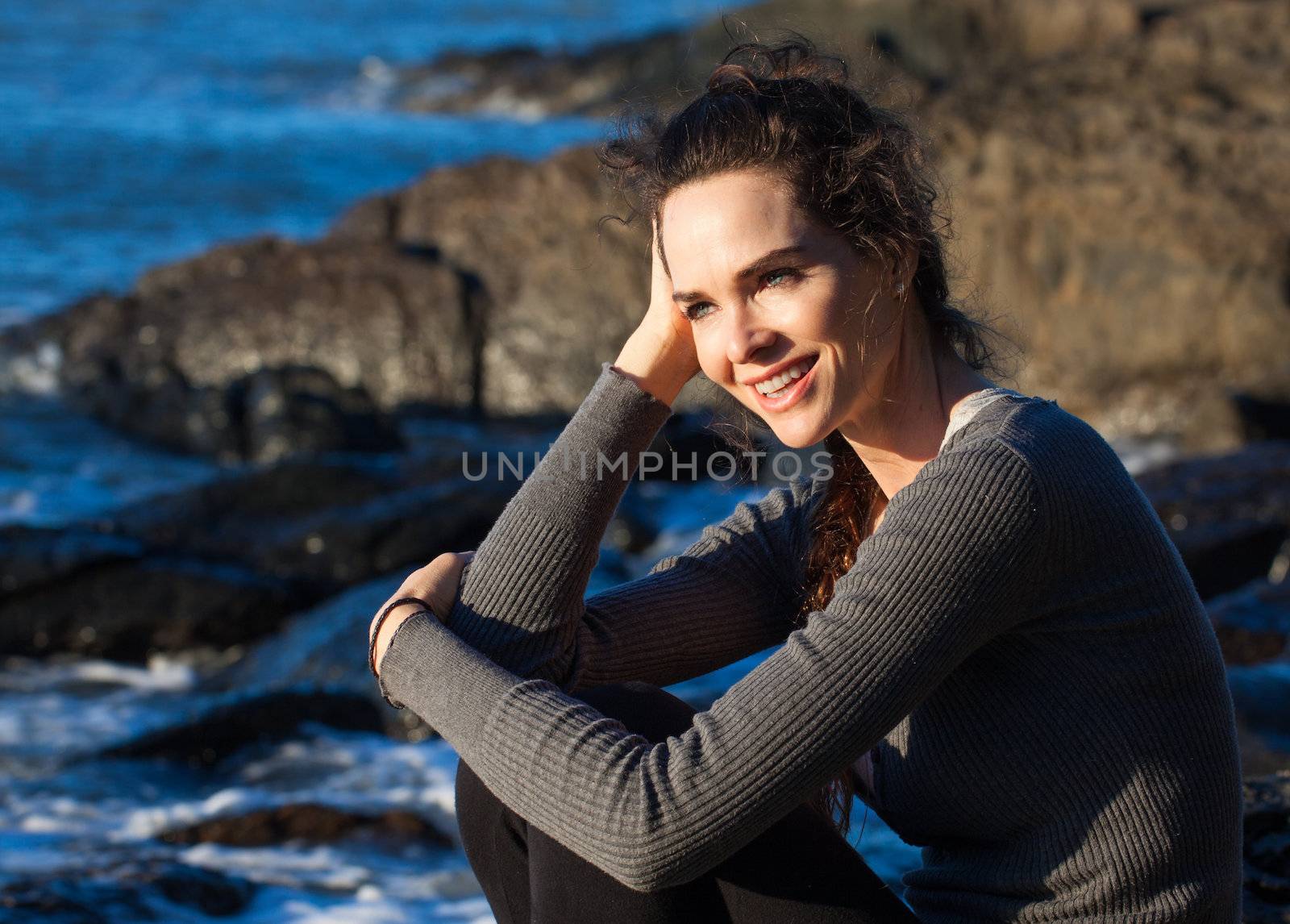 A happy smiling woman sitting by the ocean enjoying the sunshine