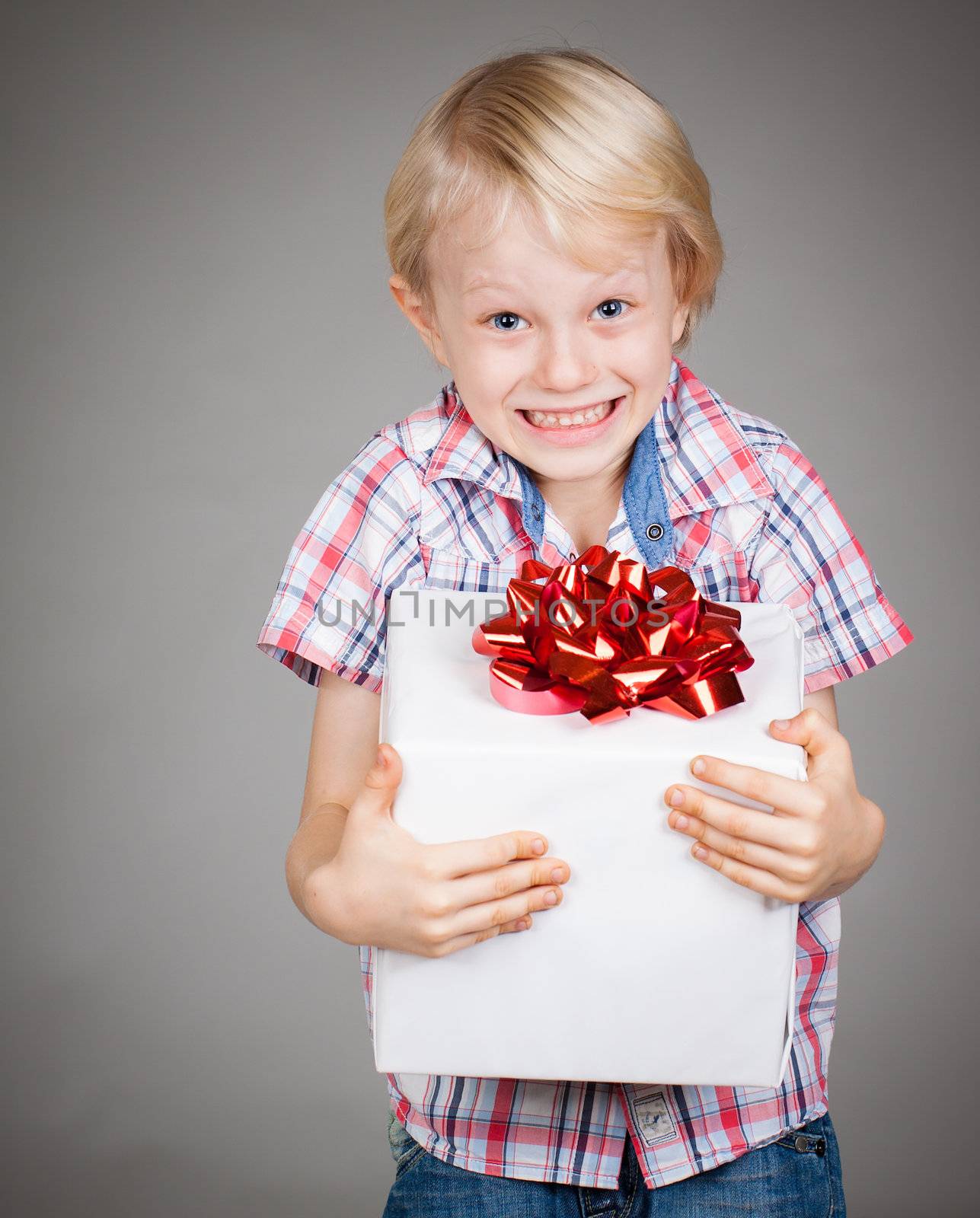 A very happy cute young boy holding a large gift or present and smiles at camera.
