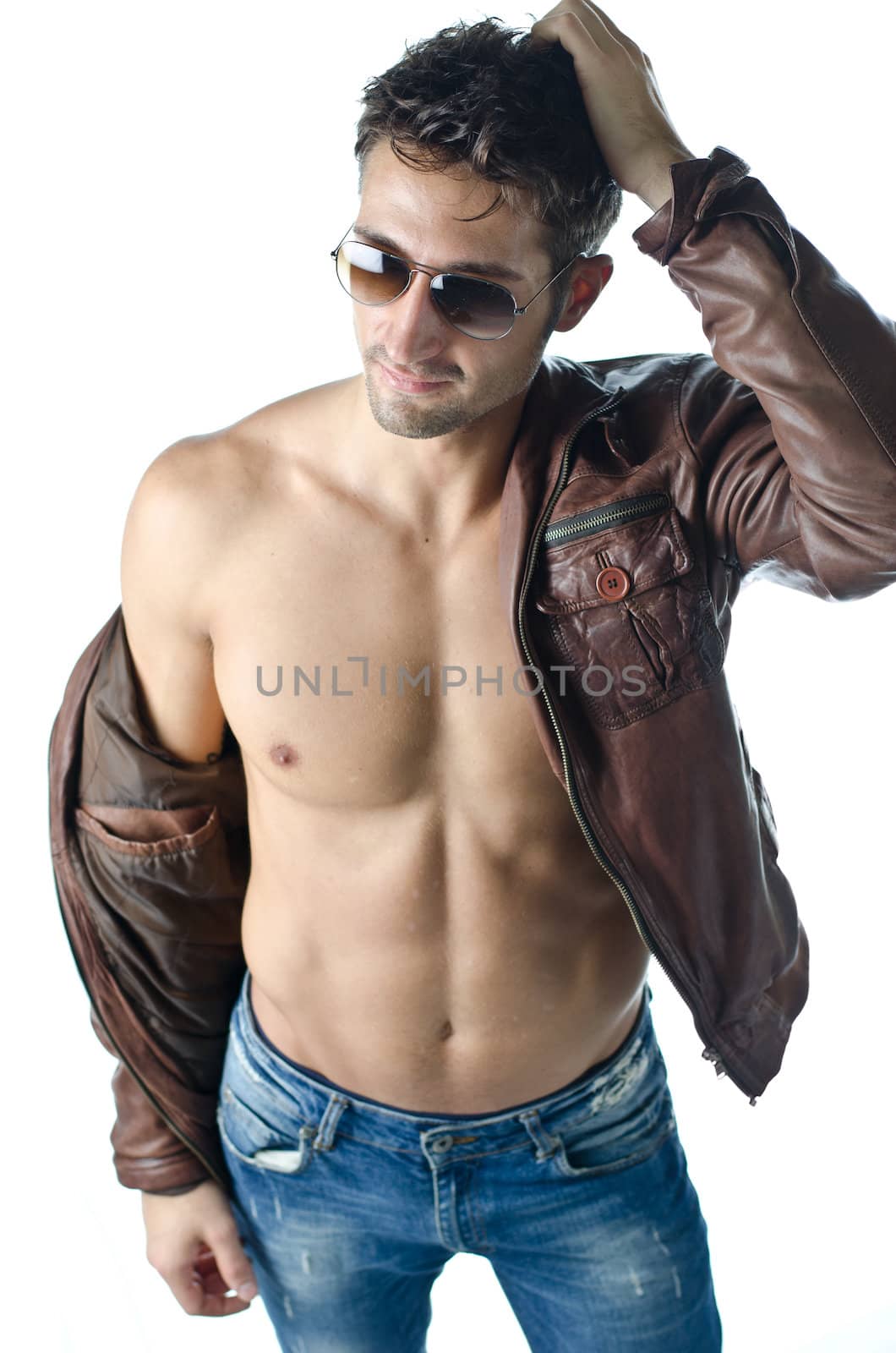 Attractive young man wearing leather jacket on naked torso and blue jeans, isolated on white