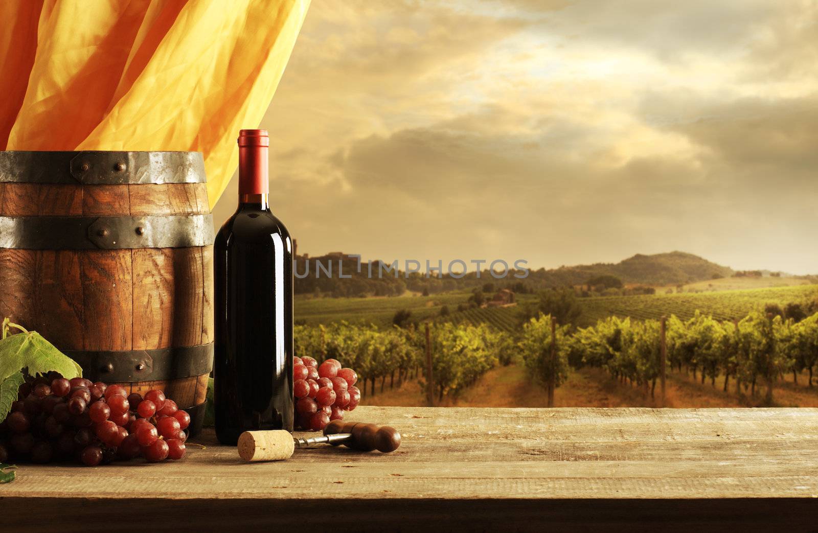 Red wine bottle, barrel and vineyard in sunset
