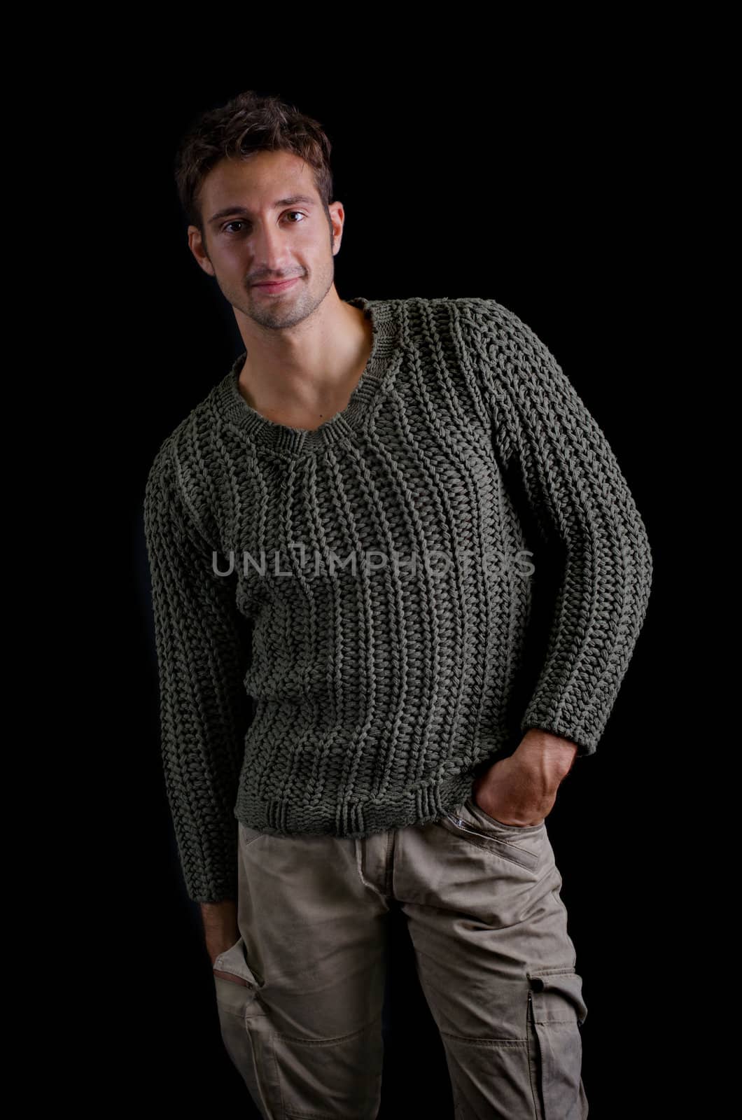 Attractive and confident young man wearing knitted sweater smiling, isolated on black