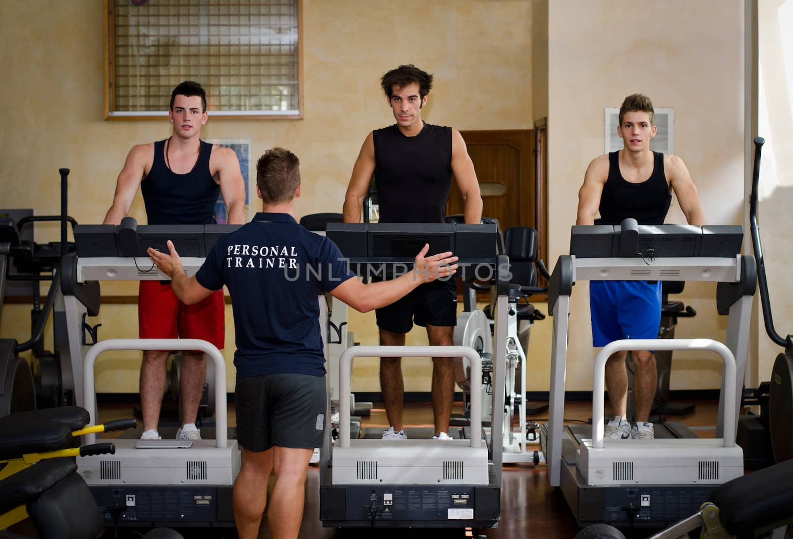 Three young men exercising on treadmills with personal trainer by artofphoto