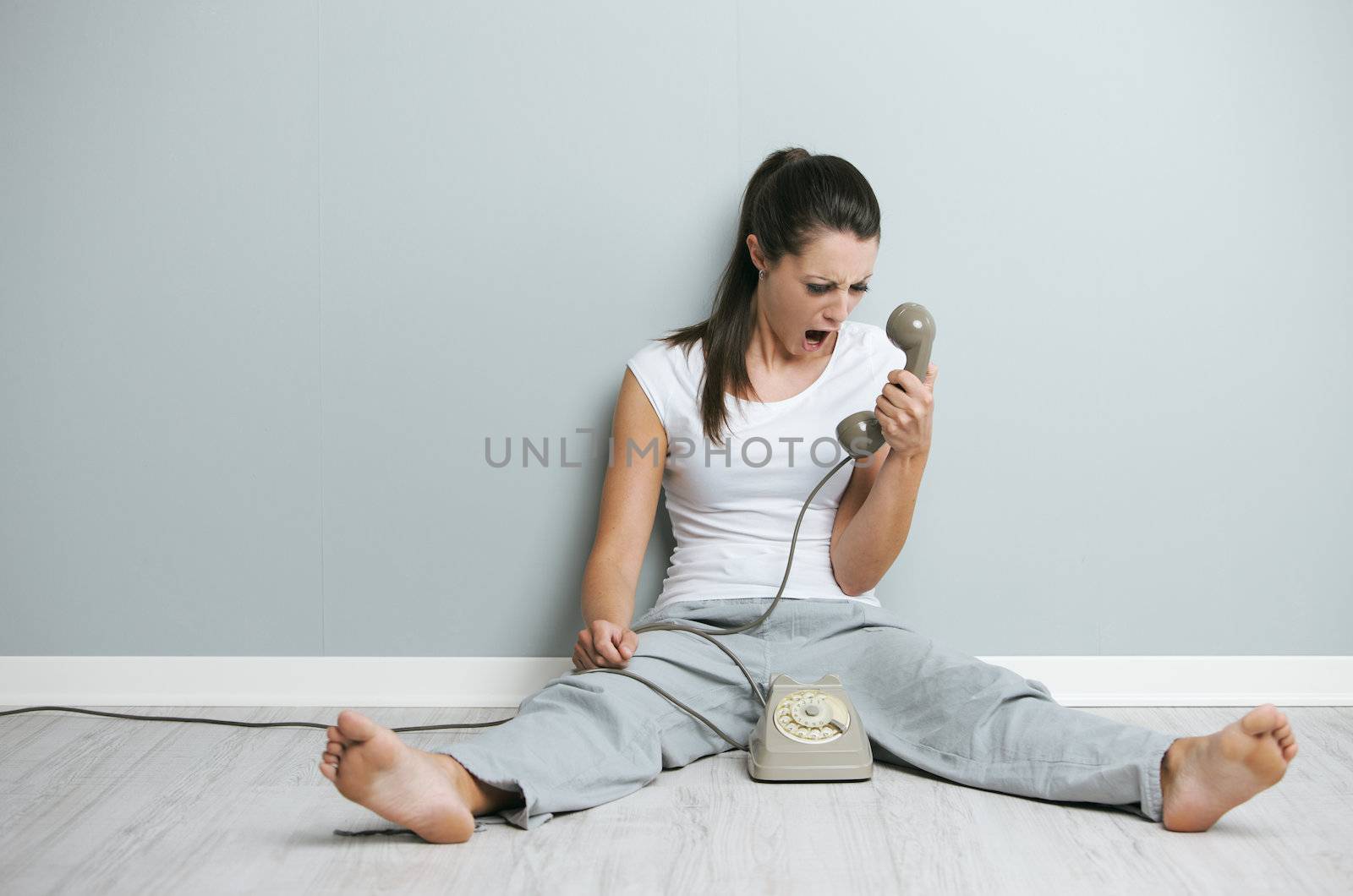 Stressed woman shouting on phone while sitting on floor