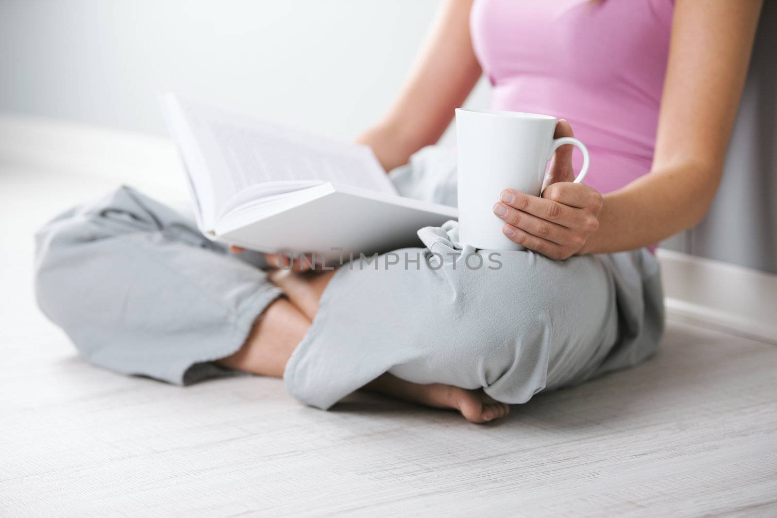 Close up of young woman with book and a cup of coffee sitting on floor