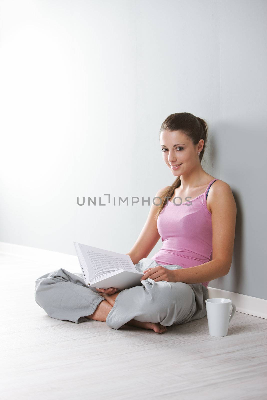 Portrait of young woman with book and a cup of coffee sitting on floor