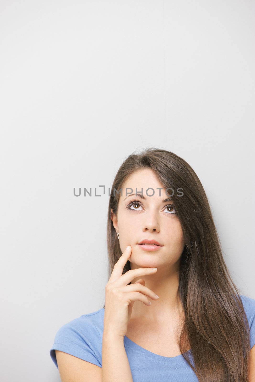 A lovely young brunette looking away thoughtfully against grey background
