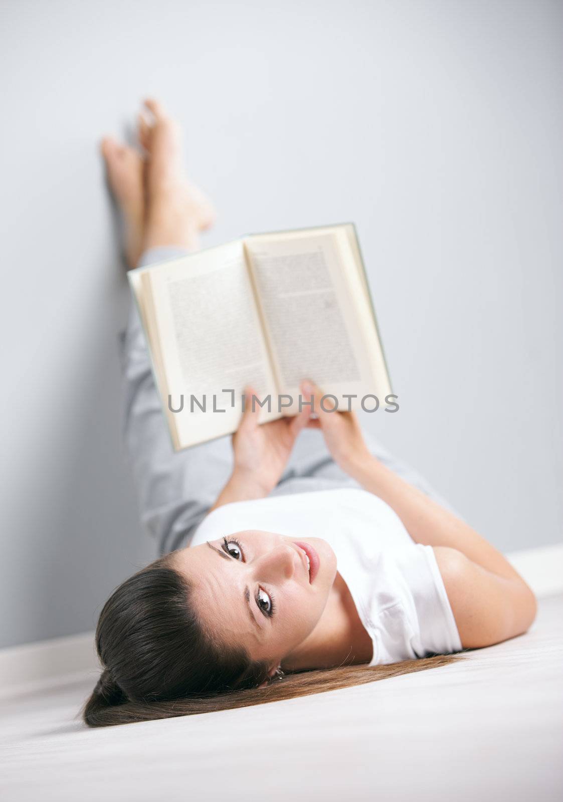 Portrait of a cute young female laying by the wall reading a book