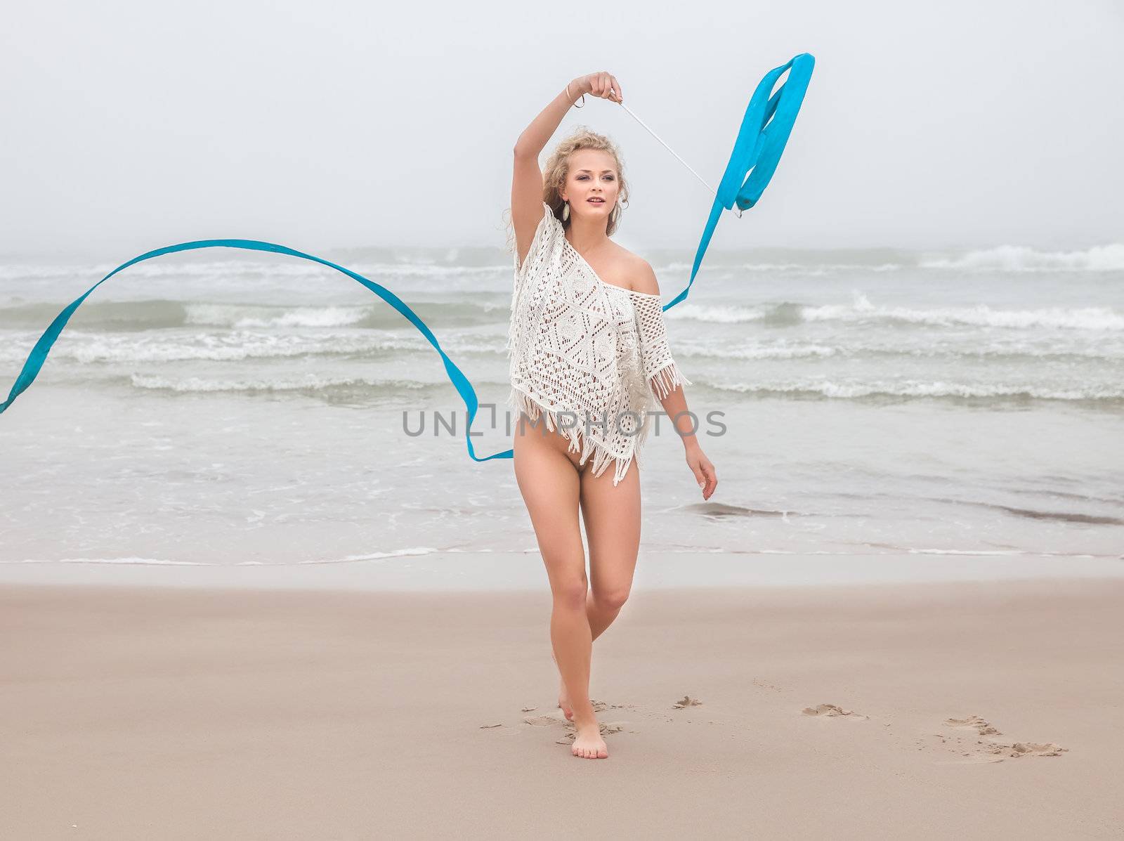 Young beautiful seminude gymnast woman dance with ribbon on the beach at foggy day