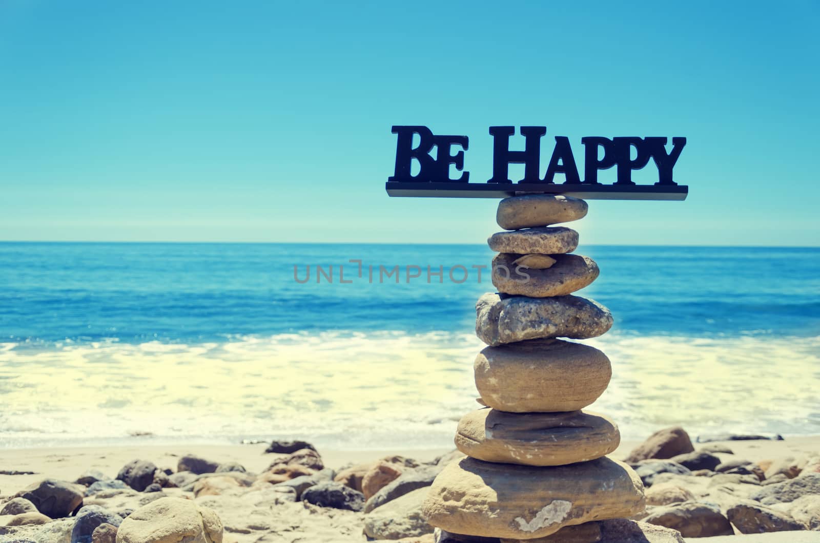 Sign "Be happy" on the top of rocks balancing by Pacific ocean - vintage